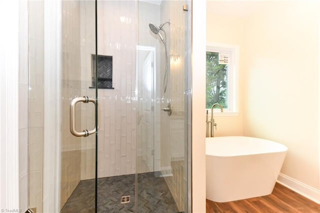 bathroom with baseboards, wood finished floors, a freestanding bath, and a stall shower