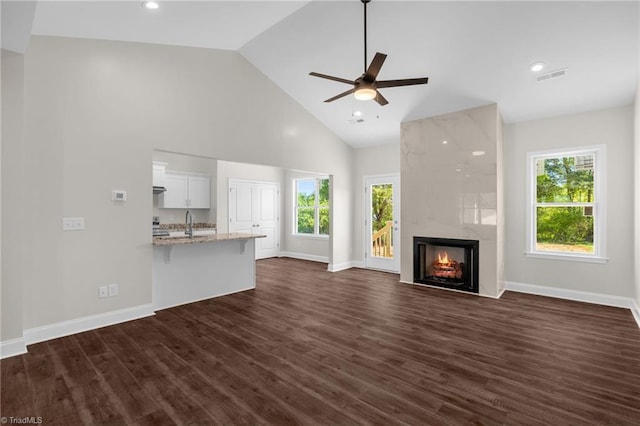 unfurnished living room featuring ceiling fan, visible vents, a premium fireplace, high vaulted ceiling, and dark wood-style flooring