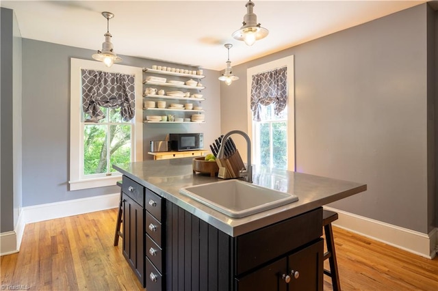 kitchen featuring pendant lighting, sink, a kitchen island, a breakfast bar, and light hardwood / wood-style flooring