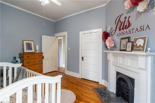 bedroom with a crib, crown molding, ceiling fan, hardwood / wood-style flooring, and a closet