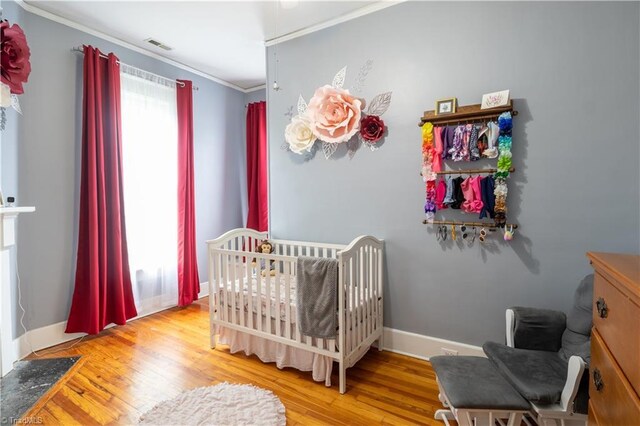 bedroom featuring a crib, crown molding, and hardwood / wood-style flooring