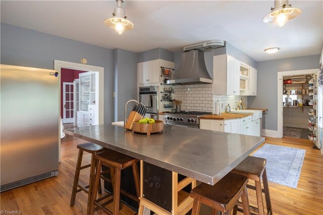 kitchen featuring wall chimney range hood, white cabinets, butcher block countertops, high end appliances, and backsplash