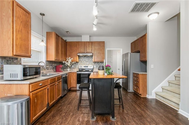 kitchen featuring a kitchen breakfast bar, stainless steel appliances, decorative light fixtures, a center island, and dark hardwood / wood-style floors