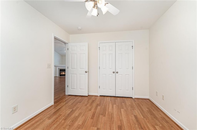 unfurnished bedroom with baseboards, a lit fireplace, a closet, and light wood finished floors