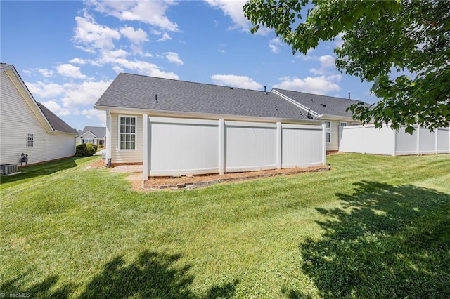 rear view of house with a lawn, fence, and a shingled roof