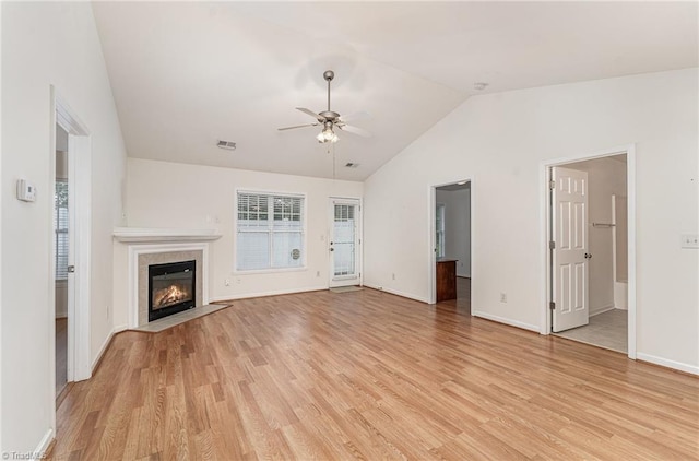 unfurnished living room featuring a tiled fireplace, a ceiling fan, baseboards, lofted ceiling, and light wood-type flooring