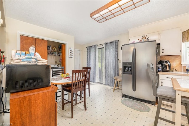 kitchen with stainless steel fridge, white cabinetry, and a textured ceiling