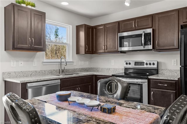 kitchen featuring light stone countertops, dark brown cabinetry, stainless steel appliances, and a sink