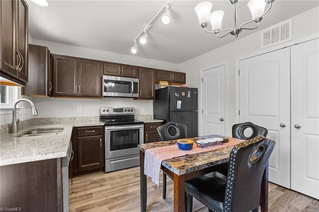 kitchen featuring light wood finished floors, visible vents, appliances with stainless steel finishes, hanging light fixtures, and a sink