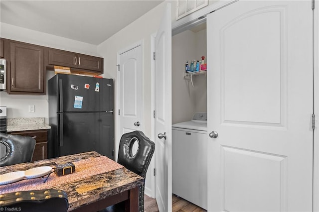 kitchen with stainless steel microwave, freestanding refrigerator, dark brown cabinetry, wood finished floors, and washer / dryer