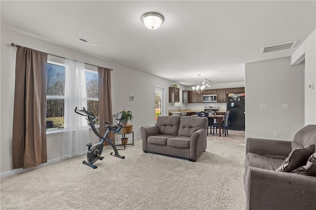 living area featuring light colored carpet, visible vents, and a notable chandelier