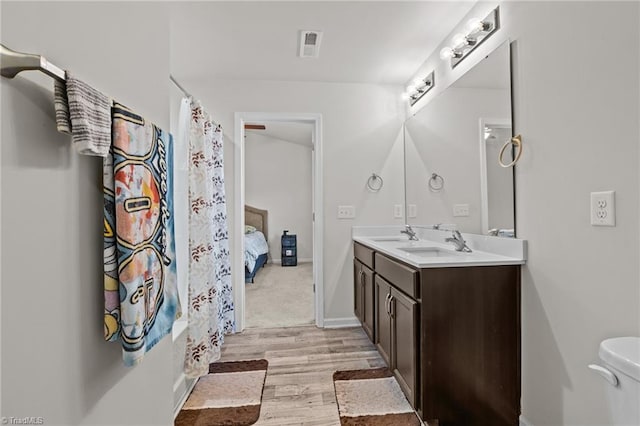 ensuite bathroom with double vanity, visible vents, connected bathroom, a sink, and wood finished floors