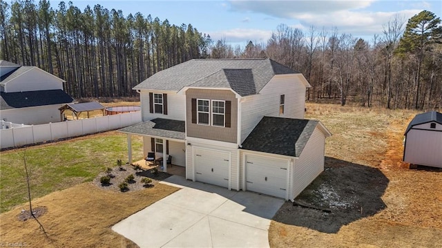 traditional-style home with fence, concrete driveway, roof with shingles, a front lawn, and a view of trees