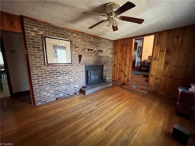 unfurnished living room with hardwood / wood-style floors, wooden walls, ceiling fan, and brick wall