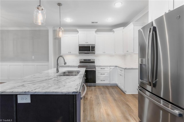 kitchen with stainless steel appliances, sink, a center island with sink, white cabinetry, and hanging light fixtures