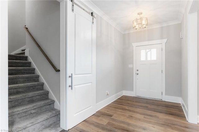 entrance foyer featuring a barn door, ornamental molding, a chandelier, and hardwood / wood-style flooring