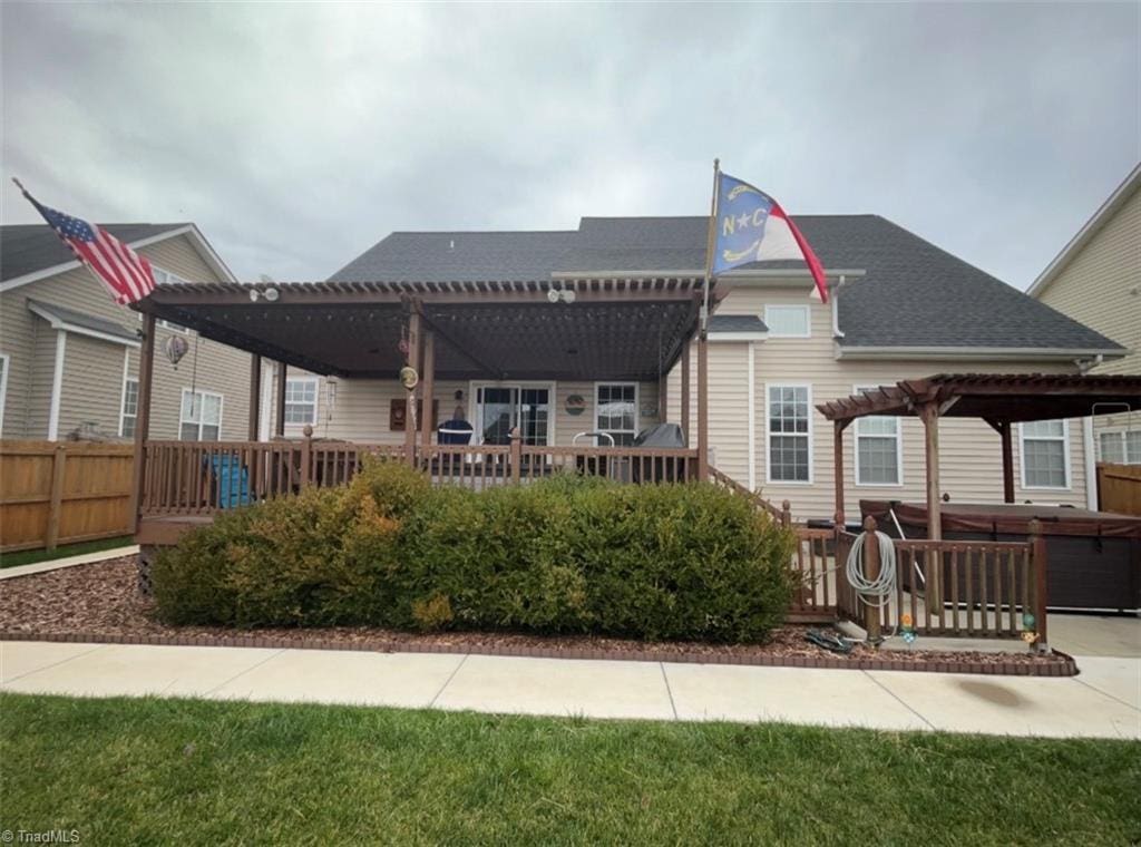 rear view of property with a pergola, fence, a shingled roof, a wooden deck, and a hot tub