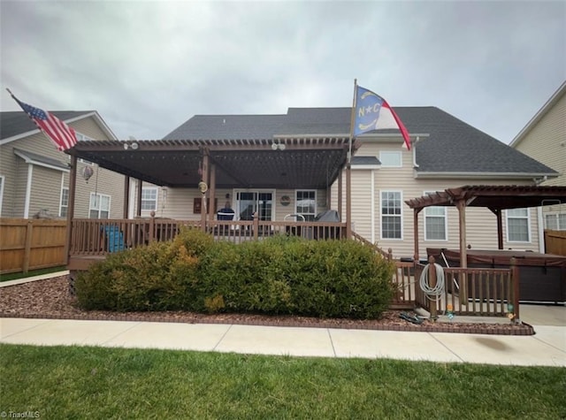 back of property with a hot tub, fence, roof with shingles, a deck, and a pergola