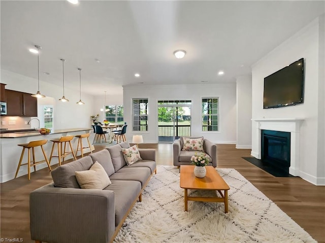 living area with wood finished floors, baseboards, a fireplace with flush hearth, and recessed lighting