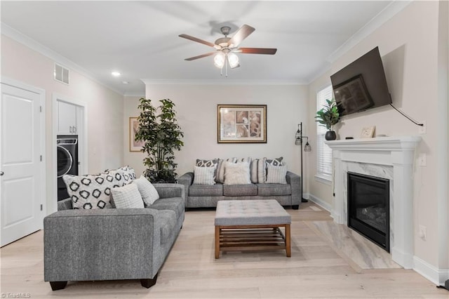 living room with a high end fireplace, light wood-type flooring, ornamental molding, ceiling fan, and washer / clothes dryer