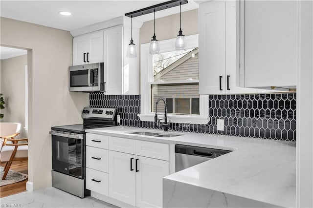 kitchen featuring a sink, decorative light fixtures, backsplash, white cabinetry, and appliances with stainless steel finishes