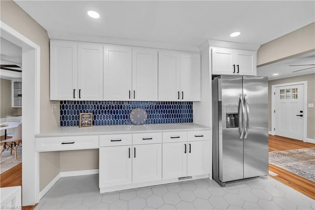 kitchen featuring decorative backsplash, stainless steel fridge, white cabinetry, and light countertops