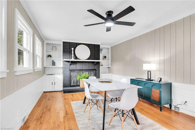 dining space with visible vents, built in shelves, light wood-style flooring, crown molding, and a brick fireplace