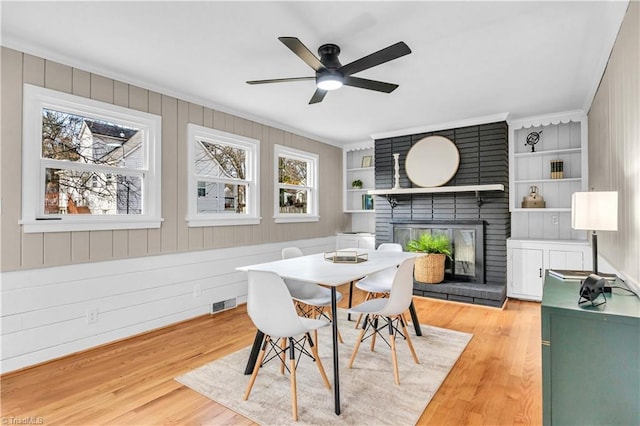 dining area featuring visible vents, built in features, a fireplace, wood finished floors, and a ceiling fan