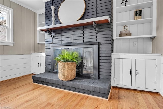 interior details featuring wood finished floors, crown molding, built in shelves, and a fireplace