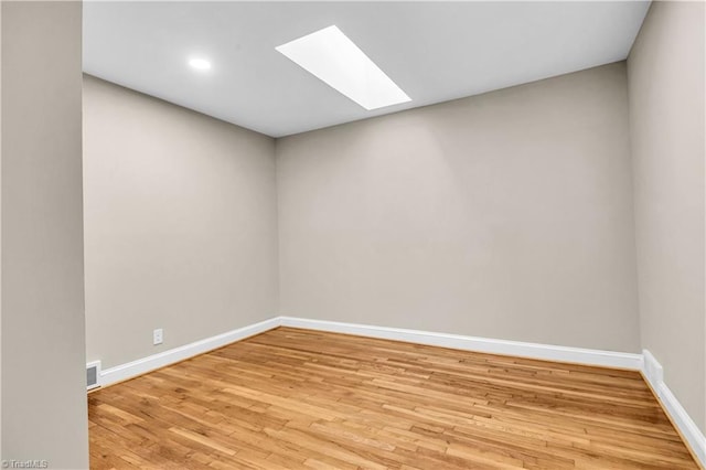 unfurnished room featuring visible vents, a skylight, baseboards, and wood finished floors