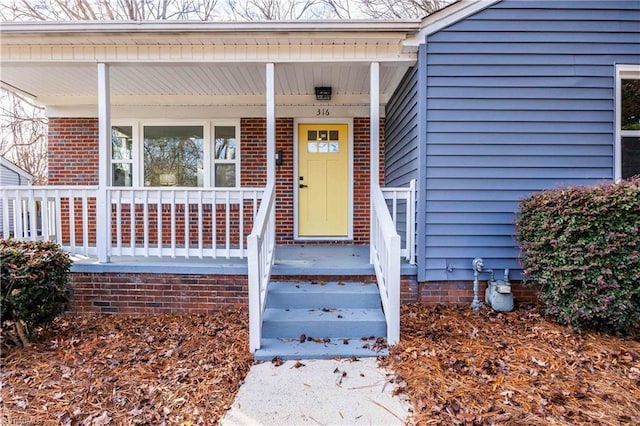 doorway to property with brick siding and covered porch