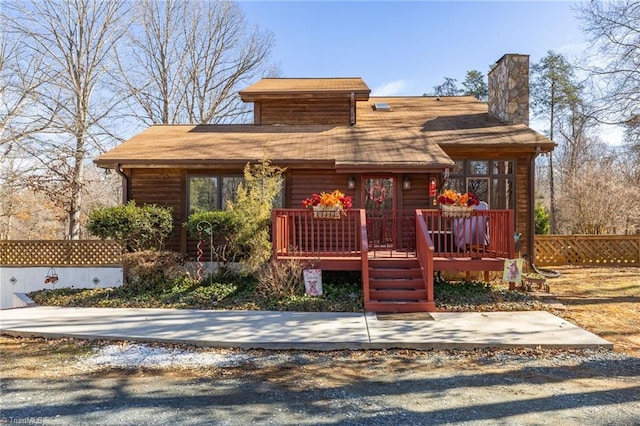 chalet / cabin with driveway, a chimney, and fence