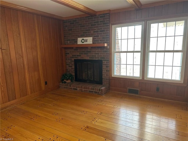 unfurnished living room featuring wooden walls, beam ceiling, and light hardwood / wood-style flooring