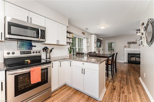 1896 Winds Dr, Winston-Salem, NC 27127 - kitchen featuring appliances with stainless steel finishes, a peninsula, a glass covered fireplace, and light wood-type flooring