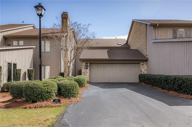 view of front of property featuring stone siding, roof with shingles, an attached garage, and driveway