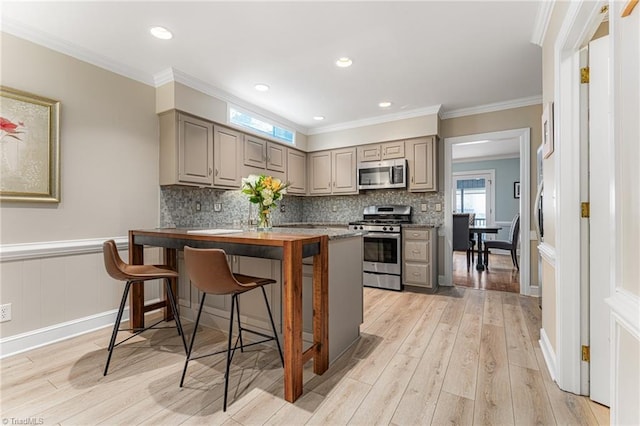 kitchen featuring light wood finished floors, a kitchen bar, appliances with stainless steel finishes, and gray cabinets