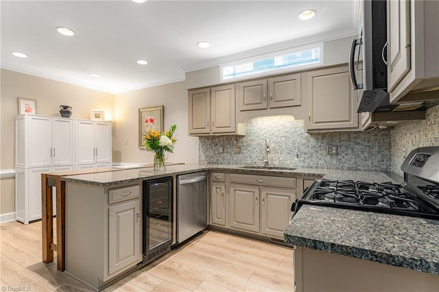 kitchen featuring beverage cooler, appliances with stainless steel finishes, ornamental molding, a peninsula, and a sink