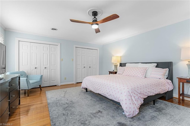 bedroom featuring light wood-style floors, visible vents, ornamental molding, and multiple closets