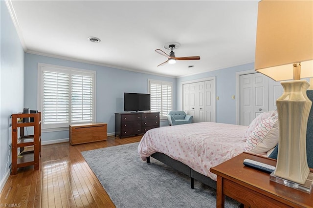 bedroom featuring visible vents, baseboards, hardwood / wood-style floors, crown molding, and multiple closets