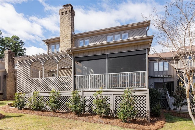 rear view of house with board and batten siding, a sunroom, a chimney, and a pergola