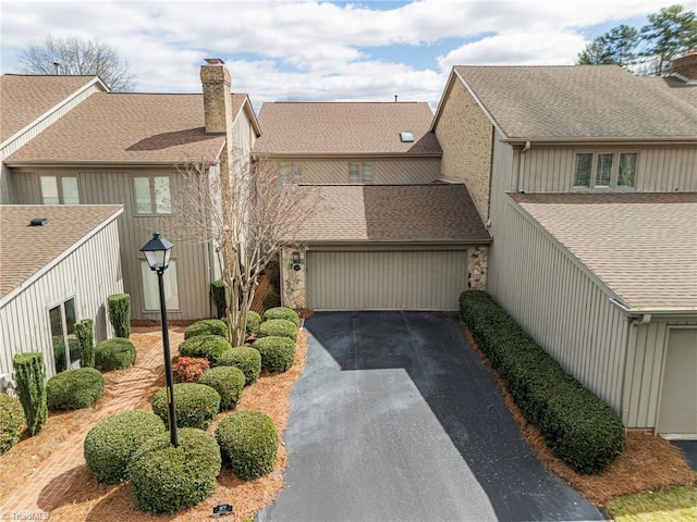 townhome / multi-family property with aphalt driveway, stone siding, a shingled roof, and a chimney