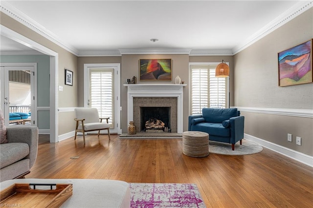 living room featuring a fireplace with raised hearth, ornamental molding, wood finished floors, and a wealth of natural light