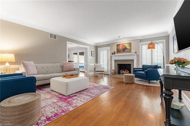 living room featuring plenty of natural light, visible vents, a fireplace with raised hearth, and hardwood / wood-style floors