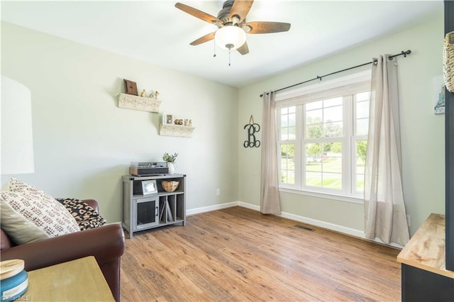 living area featuring visible vents, light wood-style flooring, baseboards, and ceiling fan