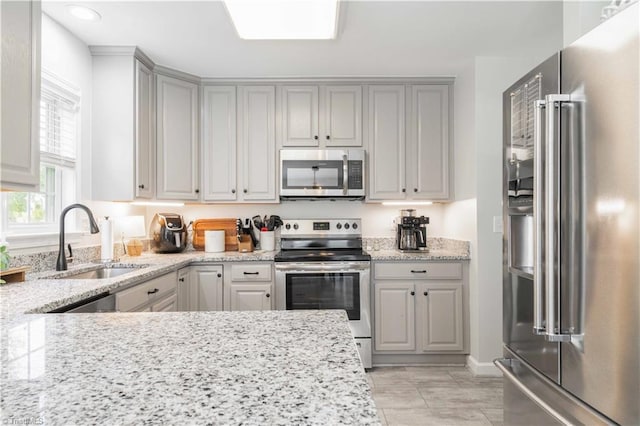 kitchen featuring light stone counters, a sink, gray cabinetry, and stainless steel appliances