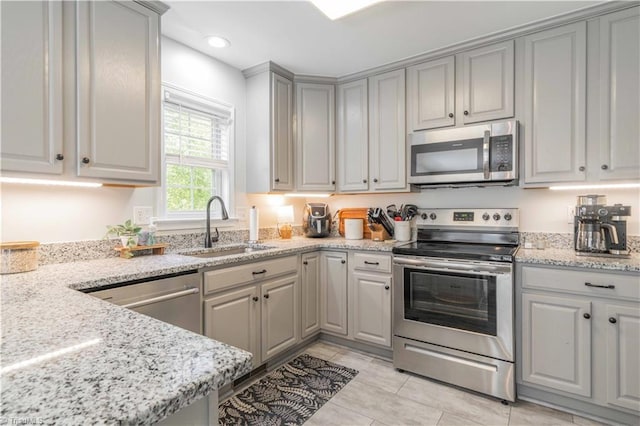 kitchen with gray cabinets, appliances with stainless steel finishes, a sink, light stone counters, and recessed lighting