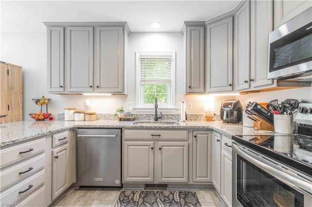 kitchen featuring light stone counters, a sink, gray cabinets, and stainless steel appliances