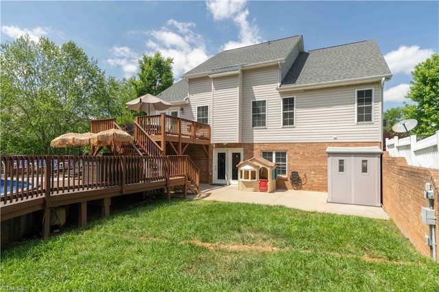 rear view of property with fence, brick siding, a wooden deck, a patio, and a yard