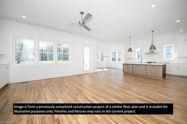 unfurnished living room featuring ceiling fan with notable chandelier, light wood-type flooring, plenty of natural light, and ornamental molding