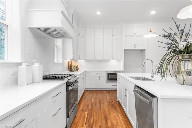 kitchen with sink, premium range hood, decorative light fixtures, white cabinets, and appliances with stainless steel finishes